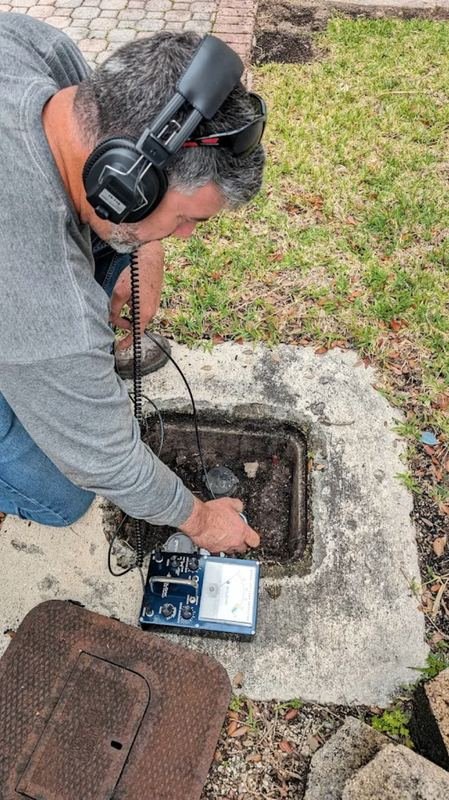 Technician using acoustic leak detection equipment at a water meter pit