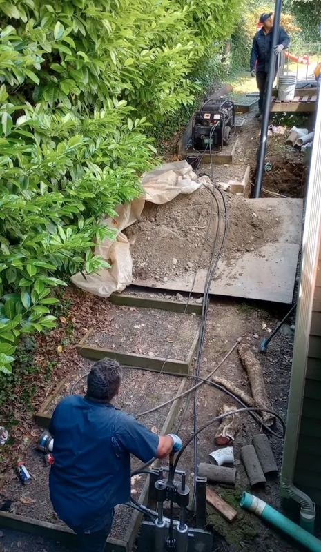 Two plumbers running a pipe bursting head along a narrow side yard